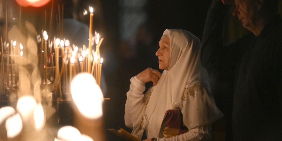 femeie care se roaga in biserica in apropierea unor lumanari